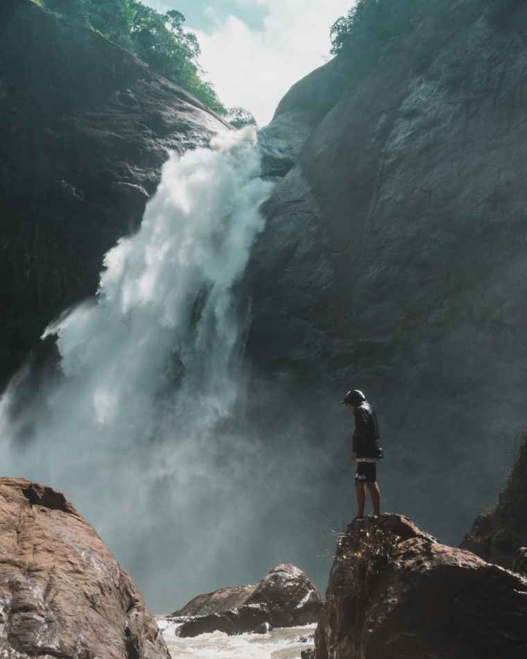 man standing on brown rock cliff in front of waterfalls photography
